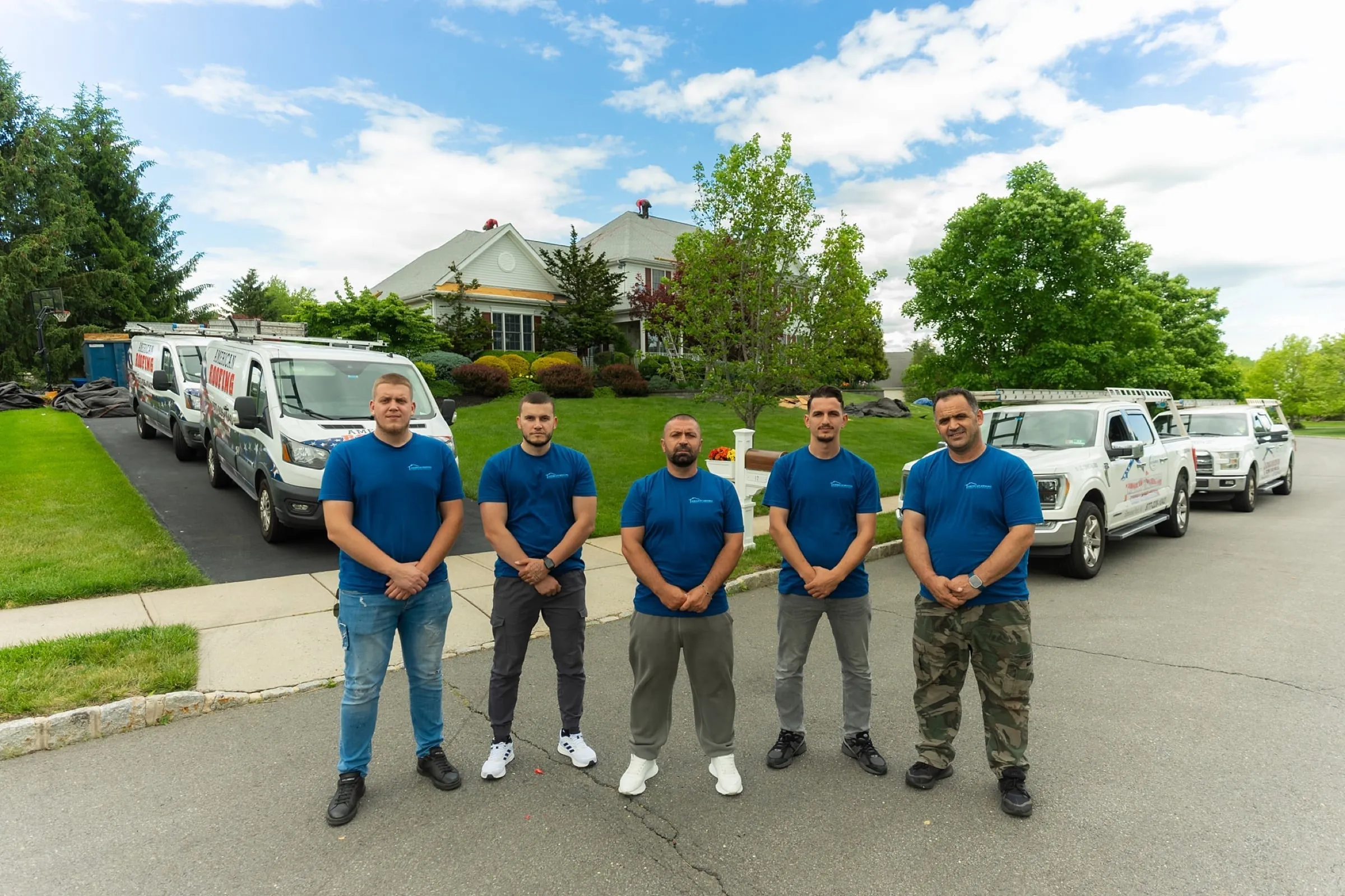 American Roofing crew standing in front of the company vans and trucks at a New Jersey job site